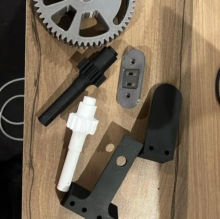 Printed drivetrain parts on a table: the spoked spur gear, pinion shafts and brackets.