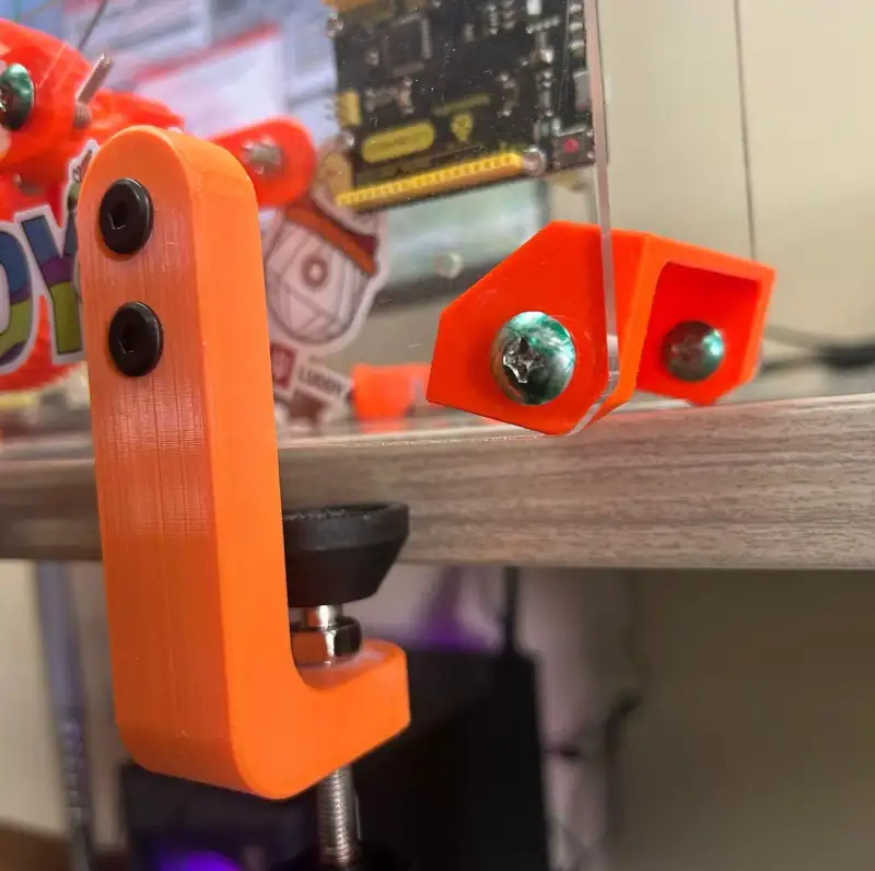 An orange printed clamp holding the kit to the edge of a desk.