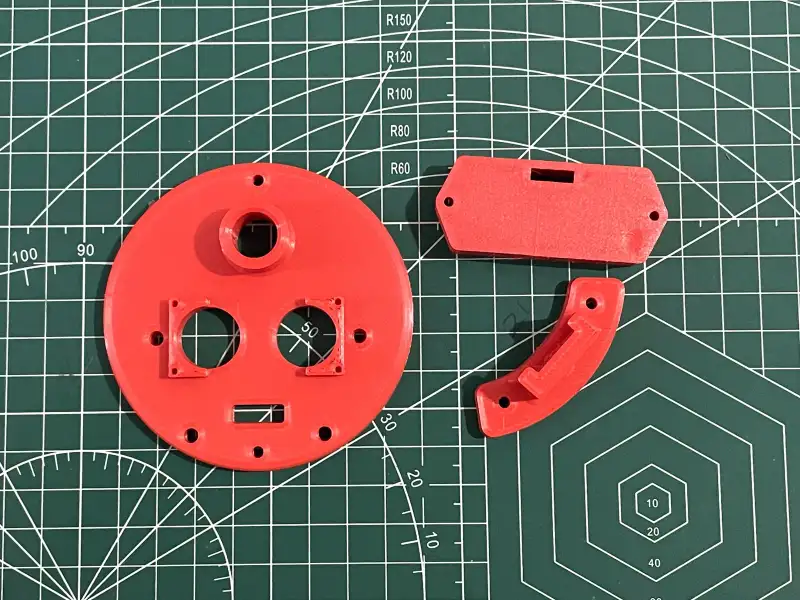 Red printed parts of the mount laid out on a cutting mat.